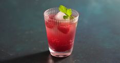 a drink with ice and strawberries in it on a black countertop next to a green leaf