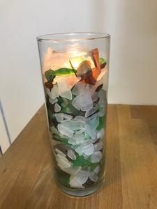 a glass filled with sea glass on top of a wooden table next to a wall