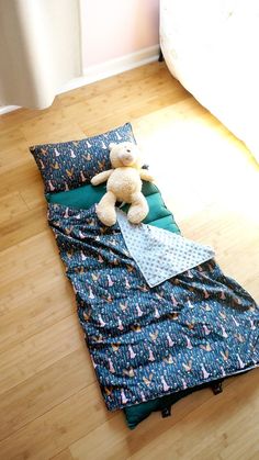 a teddy bear sitting on top of a sleeping bag in the middle of a wooden floor