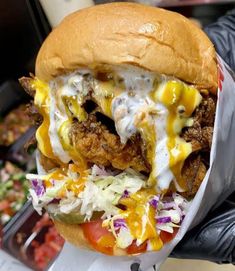 a chicken sandwich with cheese and coleslaw on it is held in a glove