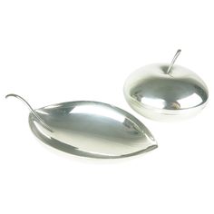 two metal spoons sitting next to each other on a white surface with an apple shaped object in the middle