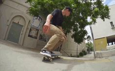 a man riding a skateboard down the side of a street next to a tree