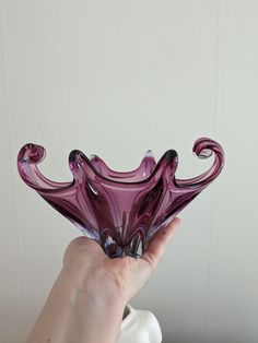 a hand holding a purple glass vase in front of a white wall