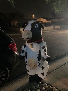 a cow mascot standing on the side of a road next to a parked car at night