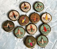 six embroidered badges with people on them sitting on a white cloth covered surface, all in different colors and sizes