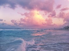 the sun is setting over the ocean with waves coming in to shore and people walking on the beach