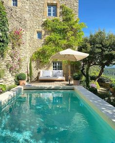 an outdoor swimming pool surrounded by greenery and stone buildings with patio furniture, umbrellas and flowers