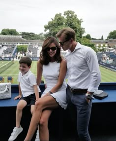 a man and woman are sitting on a bench at a tennis match with their son