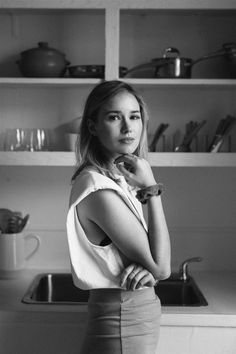 a black and white photo of a woman standing in front of a kitchen sink with her hands on her chin