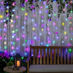 a wooden bench sitting next to a wall covered in plants and flowers with colorful lights on it