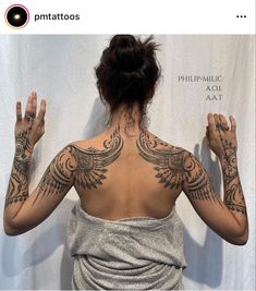 the back of a woman with tattoos on her upper and lower arms, standing in front of a white backdrop