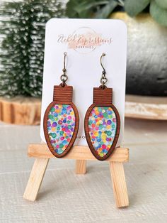 a pair of wooden earrings with multicolored dots on them sitting on a stand