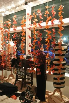 an assortment of mannequins are displayed in front of a window with fall leaves