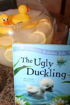 there is a book about the ugly duckling and a yellow rubber duck floating in a bowl