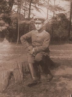 an old photo of a man in uniform sitting on a tree stump with his hands on his hips