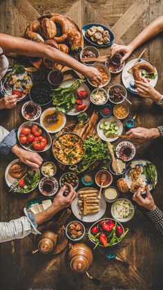 people sitting around a table full of food and plates with their hands on the plate