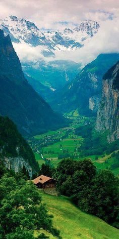 the mountains are covered in snow and green grass, with a small house on top