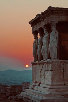 the sun is setting behind some statues on top of a hill with mountains in the background