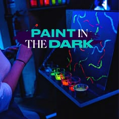 a woman is painting in the dark with neon colors on it and there are glasses next to her