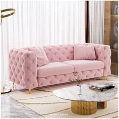 a living room with a pink velvet couch and marble coffee table in front of the window