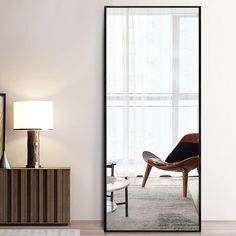 an empty living room with a chair, lamp and large mirror on the wall in front of it