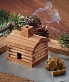 a small wooden house sitting on top of a table next to some logs and pine cones