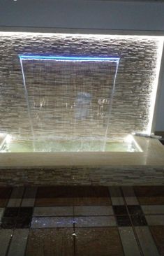 an indoor fountain is lit up in the middle of a tiled floor with water running down it