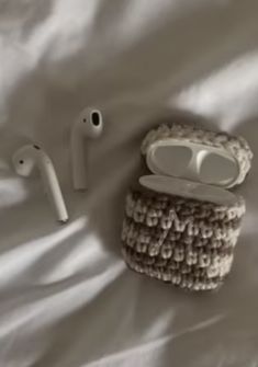 an apple airpods, headphones and case on a white sheeted bed spread