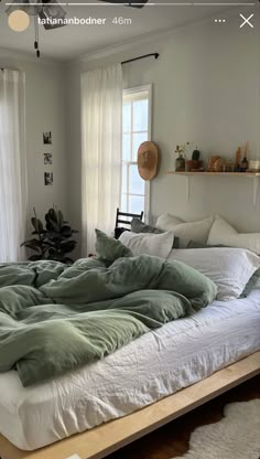 an unmade bed sitting in a bedroom next to a window with white drapes