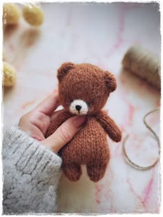 a person holding a small brown teddy bear in their left hand and knitting needles on the other