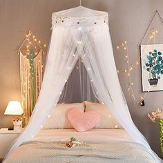 a white canopy bed in a bedroom with string lights on the ceiling and pink pillows