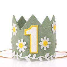 a green felt crown with white daisies and the number one on it's side