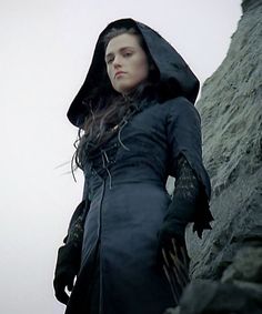 a woman dressed in black standing next to a rock