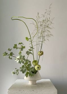 an arrangement of flowers in a white vase on a stone block against a gray wall