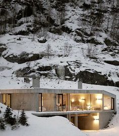 the house is surrounded by snow and trees in the mountainside area, with its lights on