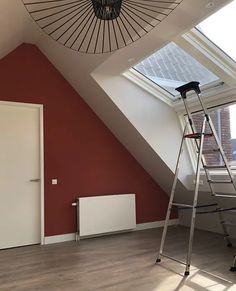 a ladder is standing in front of a red wall with a skylight above it