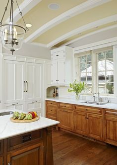 a white kitchen with wooden cabinets and marble counter tops is pictured in this image, there are many vegetables on the cutting board next to the sink