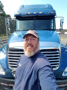 a man standing in front of a blue semi - truck with his arms out to the side