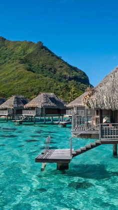 the water is crystal blue and there are huts on stilts in the water that line the shore