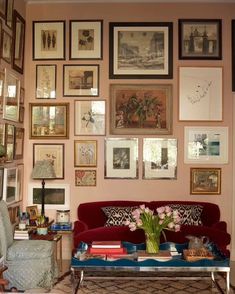 a living room filled with lots of framed pictures on the wall above a red couch