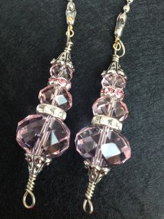 two pairs of pink crystal earrings on a black surface with silver hooks and chains hanging from them