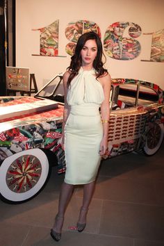 a woman in a white dress standing next to a car with wheels on the side