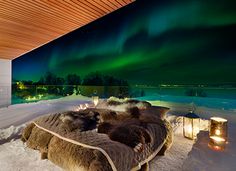 a bed sitting on top of snow covered ground under a green aurora bore in the sky