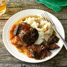 a white plate topped with meat, mashed potatoes and gravy on top of a wooden table