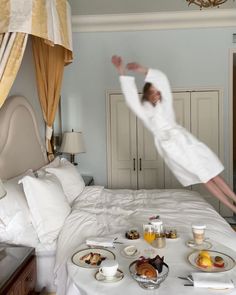 a person jumping in the air over a bed with food and drinks on top of it