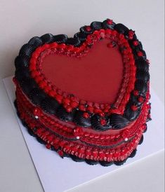 a heart - shaped cake with red and black decorations sits on top of a white card