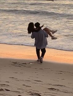 a man carrying a woman on his back as they walk along the beach at sunset