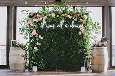 an outdoor ceremony setup with flowers and greenery on the wall, surrounded by wine barrels