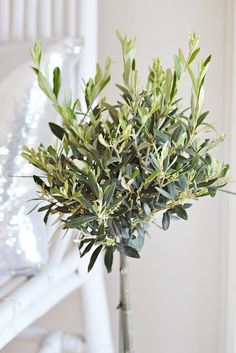 a vase filled with green leaves on top of a wooden table next to a white chair