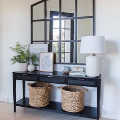 a black console table with two baskets on it and a large mirror over the top